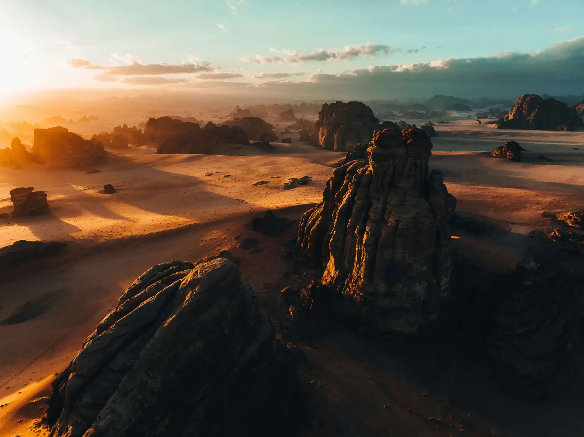 A vast rocky desert landscape at sunset, with large rock formations casting long shadows and a clear sky in the background.